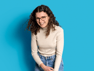 Person mit lockigem Haar und Brille vor blauem Hintergrund lächelnd.