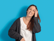Lächelnde Person vor blauem Hintergrund in einem grauen Cardigan.