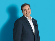 Lächelnder Mann in einem Anzug vor einem blauen Hintergrund.