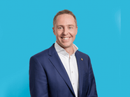 Mann in einem blauen Anzug vor einem blauen Hintergrund, lächelnd.