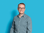 Person mit Brille und Hemd vor blauem Hintergrund.