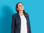 Eine Frau in einem dunkelblauen Blazer schaut vor einem blauen Hintergrund nach oben.