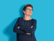 Person mit Brille und blauem Hemd vor blauem Hintergrund lächelt.