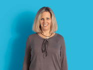 Frau mit blonder Bob-Frisur steht vor einer blauen Wand.