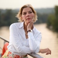 Frau lehnt nachdenklich am Geländer mit Fluss im Hintergrund.