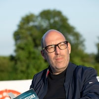 Autor Benjamin Cors sitzt auf einer Aussenterrasse und hält sein Buch Leuchtfeuer in den Händen.
