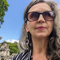 Frau mit Sonnenbrille vor Grabsteinen und blauem Himmel.