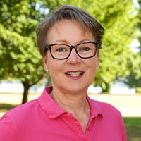 Lächelnde Frau mit Brille im Park, rosa Hemd.