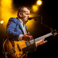 Gitarrist im blauen Anzug singt auf der Bühne.