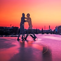 Silhouette der Molecule-Man-Skulptur auf der Spree vor Berliner Skyline im Abendrot.