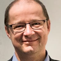 Mann mit Brille und Anzug lächelt.