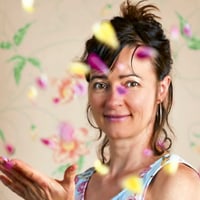Frau wirft bunte Blütenblätter vor blumiger Tapete.