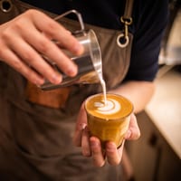Barista giesst Latte Art in einen Kaffee.