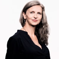 Frau mit langen Haaren lächelt vor weissem Hintergrund.