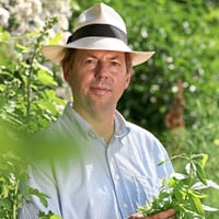 Mann mit Hut in einem Garten, von Pflanzen umgeben.