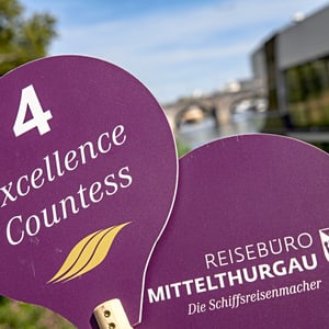 Zwei lila Schilder mit Aufschrift 'Excellence Countess' und 'Reisebüro Mittelthurgau', im Freien.