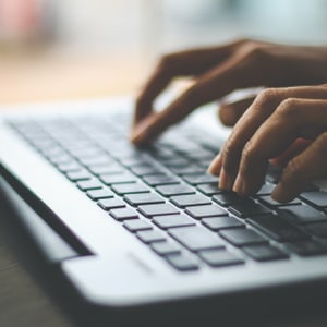Nahaufnahme von Händen, die auf einer Laptop-Tastatur tippen.