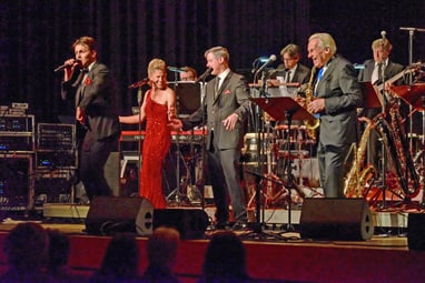 Band auf der Bühne mit Sängern und Musikern in formeller Kleidung.