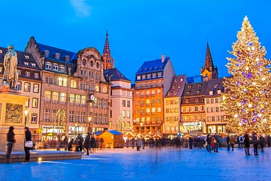 Weihnachtsbaum und Statuen auf beleuchtetem Platz bei Dämmerung.