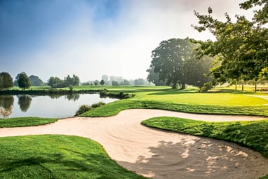 Golfplatz mit Sandbunker und Teich bei Sonnenschein.