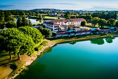 Luftaufnahme eines Gebäudes am See mit Bäumen und Landschaft.