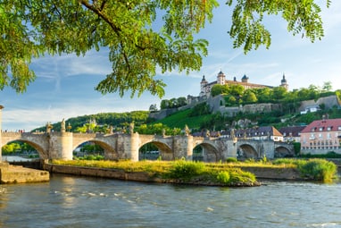 hoch-ueber-wuerzburg-thront-die-festung-marienberg.jpg Alte Steinbrücke über Fluss mit Festung im Hintergrund.