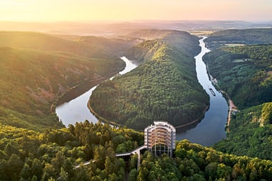 die-saarschleife-zeigt-die-naturwunder-im-naturpark-saar-hun.jpg Luftaufnahme einer Flussbiegung im bewaldeten Tal bei Sonnenuntergang.