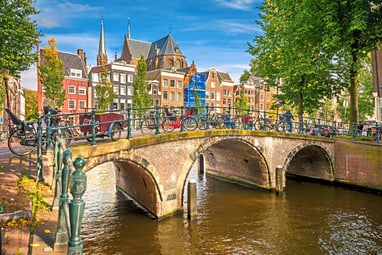 Brücke über einen Kanal in Amsterdam mit Fahrrädern und alten Gebäuden im Hintergrund.