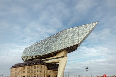 Modernes Gebäude mit gläsernem Aufbau über historischem Backsteingebäude am Wasser.