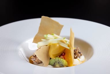 Elegantes Dessert mit Obst und knusprigen Stücken auf einem weissen Teller.