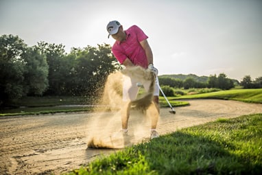 golfclub-botaniq.jpg Golfer im rosa Hemd schlägt aus einem Sandbunker.