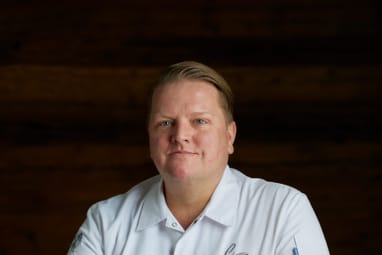 Person in weissem Kochmantel sitzt an einem Holztisch.