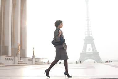 Frau in Business-Outfit geht vor dem Eiffelturm entlang.