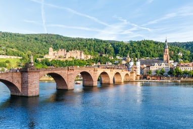 Steinbrücke über einen Fluss mit Stadt und Hügel im Hintergrund.