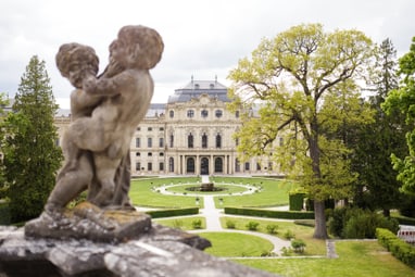 twerenbold_101989.jpg Steinfigur vor barockem Schloss mit Garten.