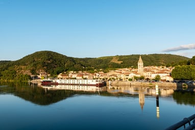 die-excellence-rhone.jpg Flusspanorama mit Dorf und Hügeln im Hintergrund.
