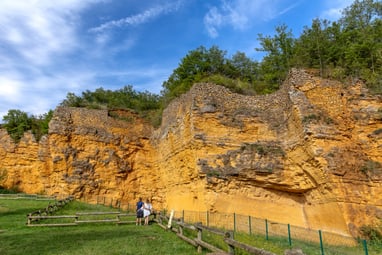 der-steinbruch-carrieres-de-glay-geologisches-unesco-welterb.jpg Besucher betrachten gelbe Steinmauer mit Bäumen oben.