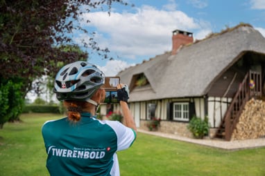 Person mit Helm fotografiert Fachwerkhaus im Grünen.
