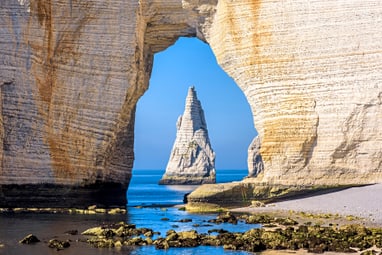 Felsentor am Meer mit freistehendem Felsen im Hintergrund.