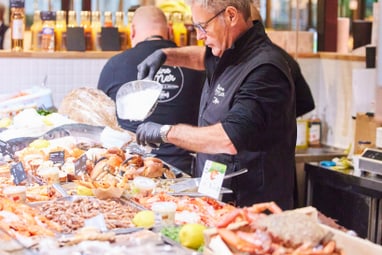 Mann hinter einer Fisch- und Meeresfrüchte-Theke auf einem Markt.