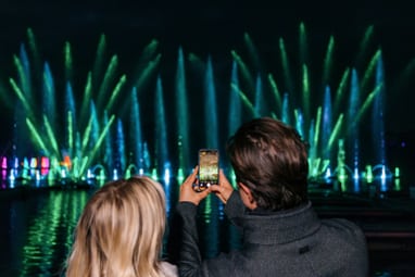Menschen fotografieren Wasserfontänen-Show bei Nacht.