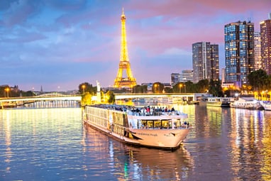 Beleuchtetes Schiff auf der Seine vor Eiffelturm bei Abenddämmerung.