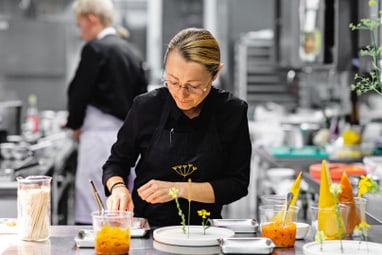 Koch in schwarzer Schürze, der in einer Restaurantküche arbeitet.