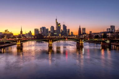 Fluss vor Stadtansicht bei Sonnenuntergang mit beleuchteten Gebäuden und Brücken.