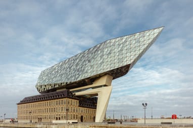 Modernes Gebäude mit glasüberdachtem Dach über historischem Backsteingebäude am Wasser.