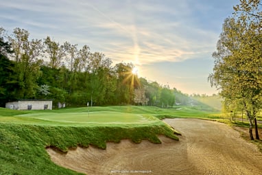 Sonnenaufgang über einem Golfplatz mit Bunker und Bäumen.