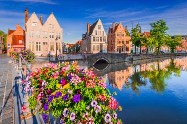 Bunte Blumen auf einer Brücke vor historischen Gebäuden am Wasser.