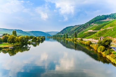 Flusslandschaft mit Hügeln und Bäumen bei sonnigem Wetter.