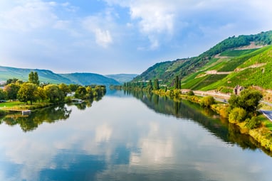 mosel.jpg Flusslandschaft mit Hügeln und Bäumen bei sonnigem Wetter.