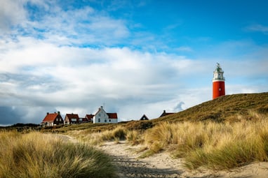 Roter Leuchtturm auf Düne mit Häusern im Hintergrund.